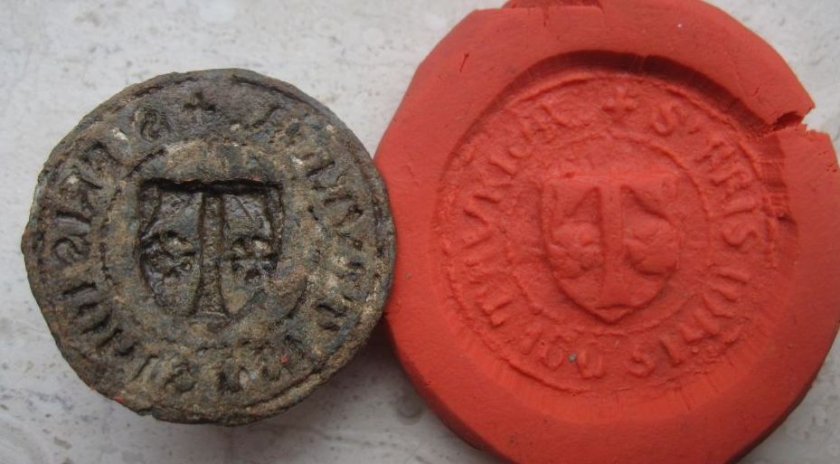 mittelalterliches Petschaft aus Blei, Umschrift in gothischen Majuskeln, im Wappen ein T, links und rechts davon jeweils 1 Blüte, etwa 14.Jh.